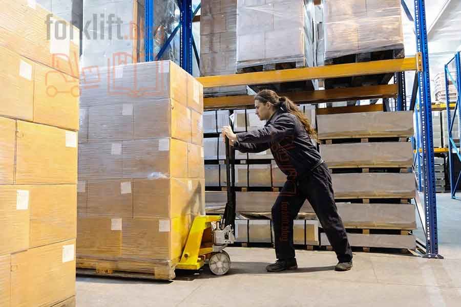 Работник склада перемещает паллету с грузом с помощью ручной гидравлической тележки (рохли) между стеллажами.