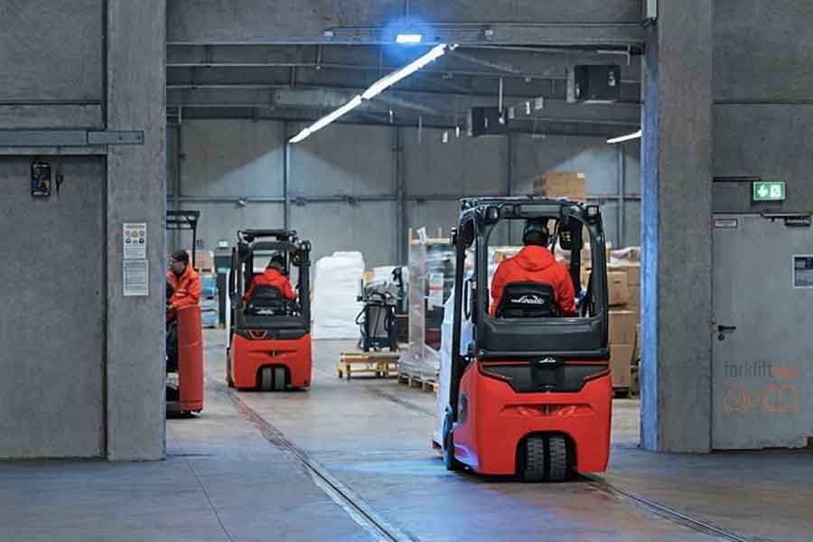 Электрические погрузчики Linde работают внутри склада, операторы в ярко-красной спецодежде перемещают грузы между паллетами и стеллажами
