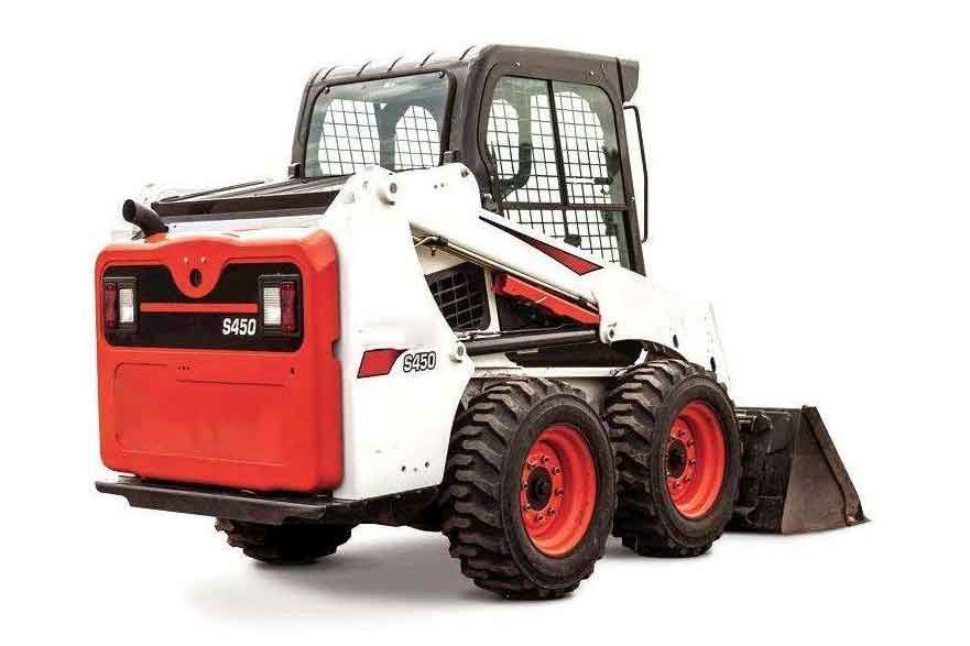 Компактный мини-погрузчик Bobcat S450 работает на строительной площадке, перевозя щебень в поднятом ковше; вокруг виден строительный грунт и техника
