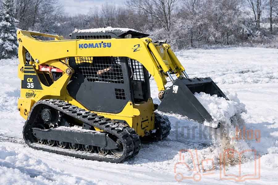 Мини-погрузчик Komatsu CK35 на гусеничном шасси работает в зимних условиях, обеспечивая надёжную производительность на снегу и пересечённой местности