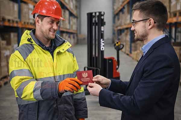 Оператор штабелера в спецодежде получает удостоверение тракториста от офисного сотрудника на территории современного склада, на заднем плане электрический штабелер SHANN