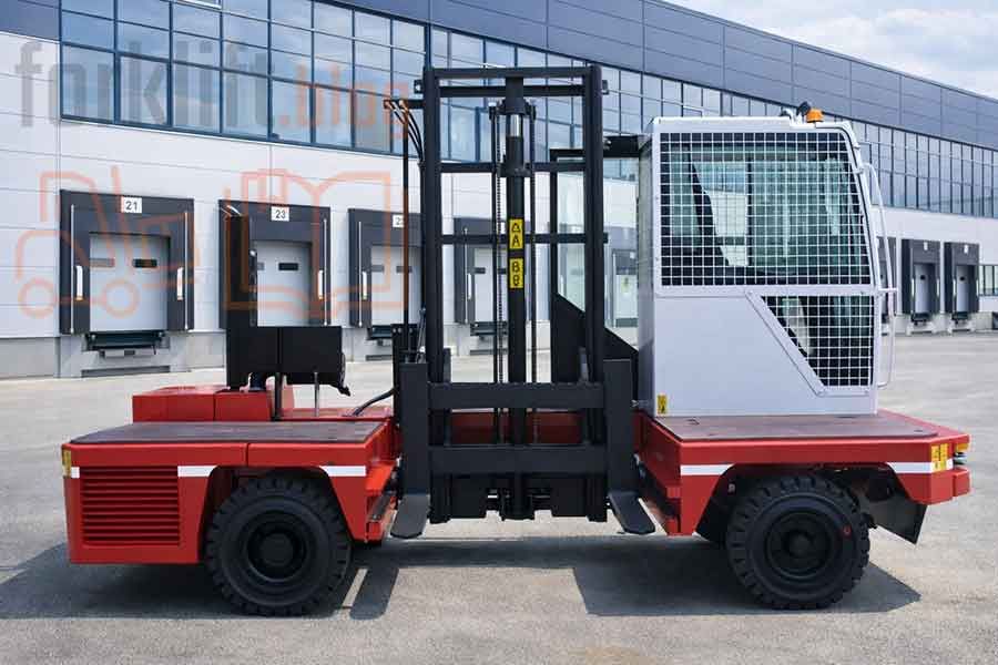 Боковой вилочный погрузчик с закрытой кабиной расположен у современного логистического центра, специализированная техника для безопасной обработки длинномерных грузов на открытых площадках.