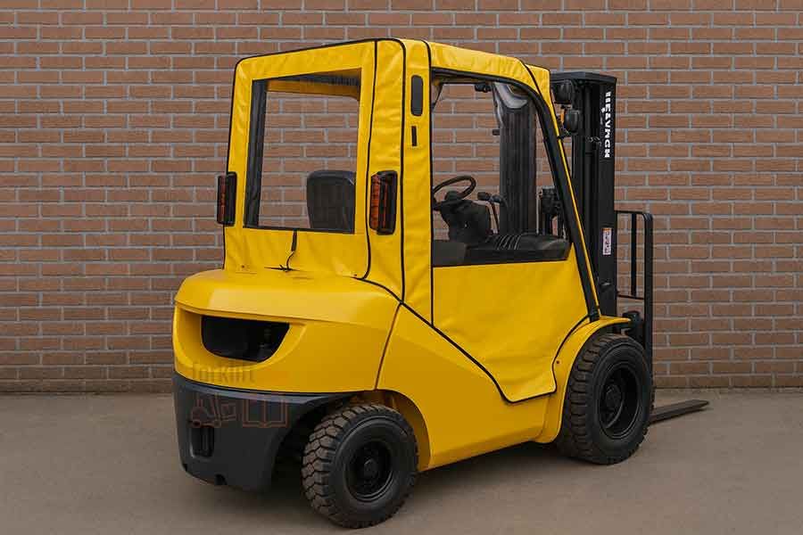 Жёлтый вилочный погрузчик с мягкой ПВХ-кабиной, стоящий на улице возле кирпичной стены.