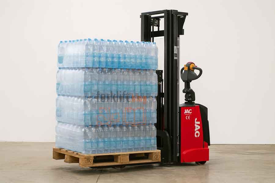 Электроштабелер JAC поднимает паллету с напитками в складском помещении, рядом двухъярусные стеллажи, на которых хранятся бутылки.